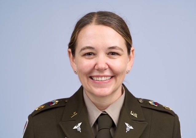 Une personne portant un uniforme militaire américain avec des insignes médicaux sourit à la caméra sur un fond bleu clair uni. Il s'agit d'Amy Thrasher, Psy.D.